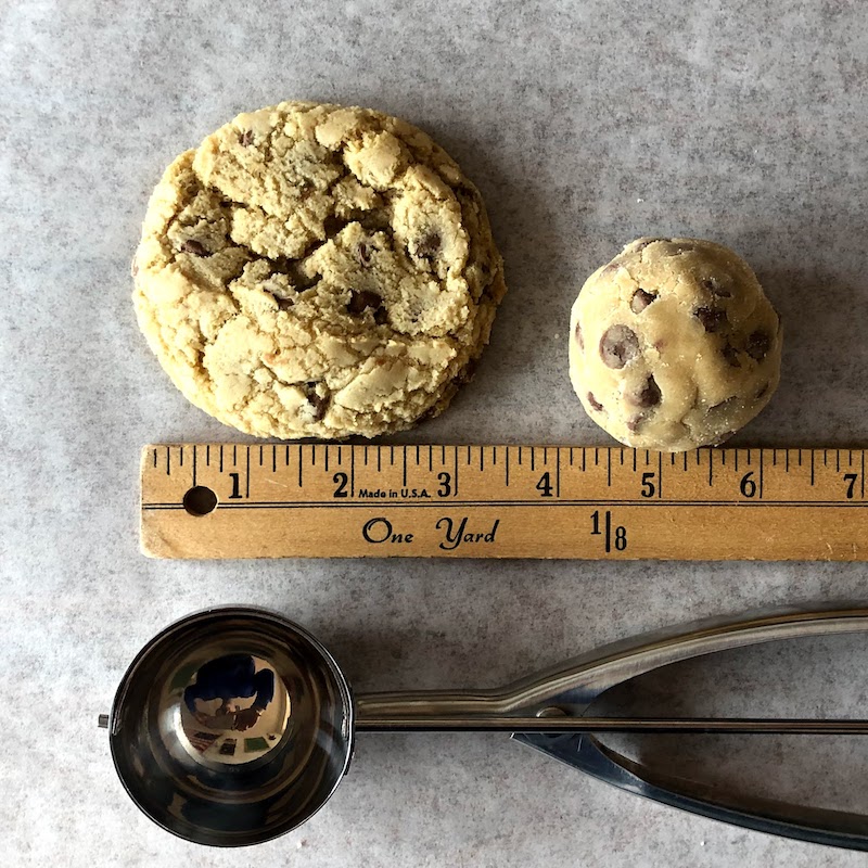 Chewy chocolate chip cookie, dough, and cookie scoop lined up next to a ruler. 