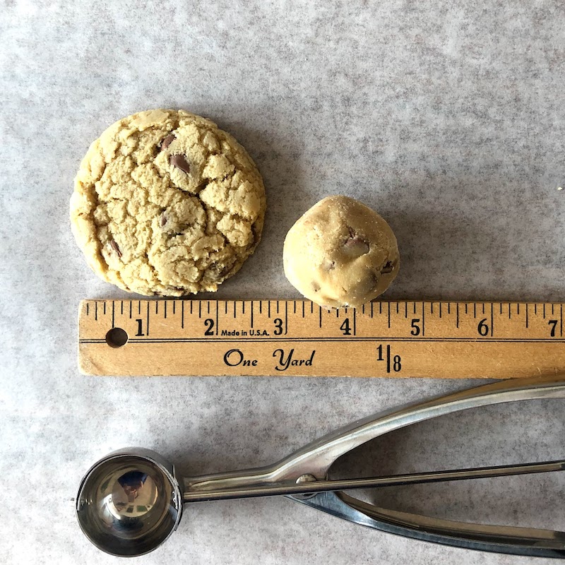 Chewy chocolate chip cookies and dough lined up next the #40 scoop and a ruler. 