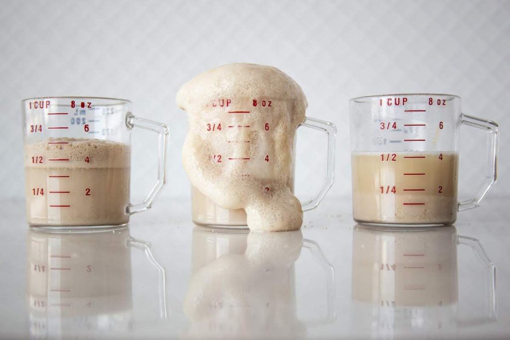 three liquid measuring cups showing the importance of water temp when proofing yeast. The first cup is 80 degree water and the yeast did not foam adequately. The second cup is 110 degree water and the foam is overflowing the cup. and the third cup is 150 degree water, which has killed the yeast and no foam has been made. 