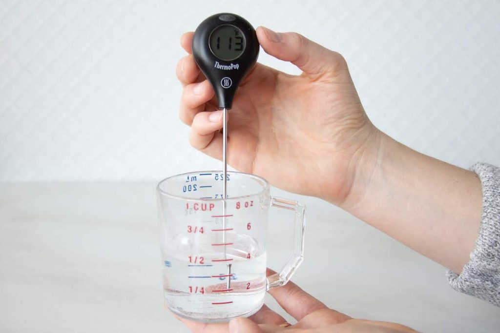 Instant read thermometer in a liquid measuring cup reading the temp 113 degrees.