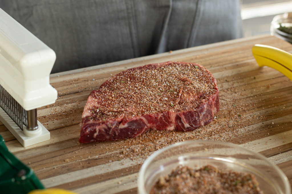 A ribeye steak is coated in rub and ready to grill