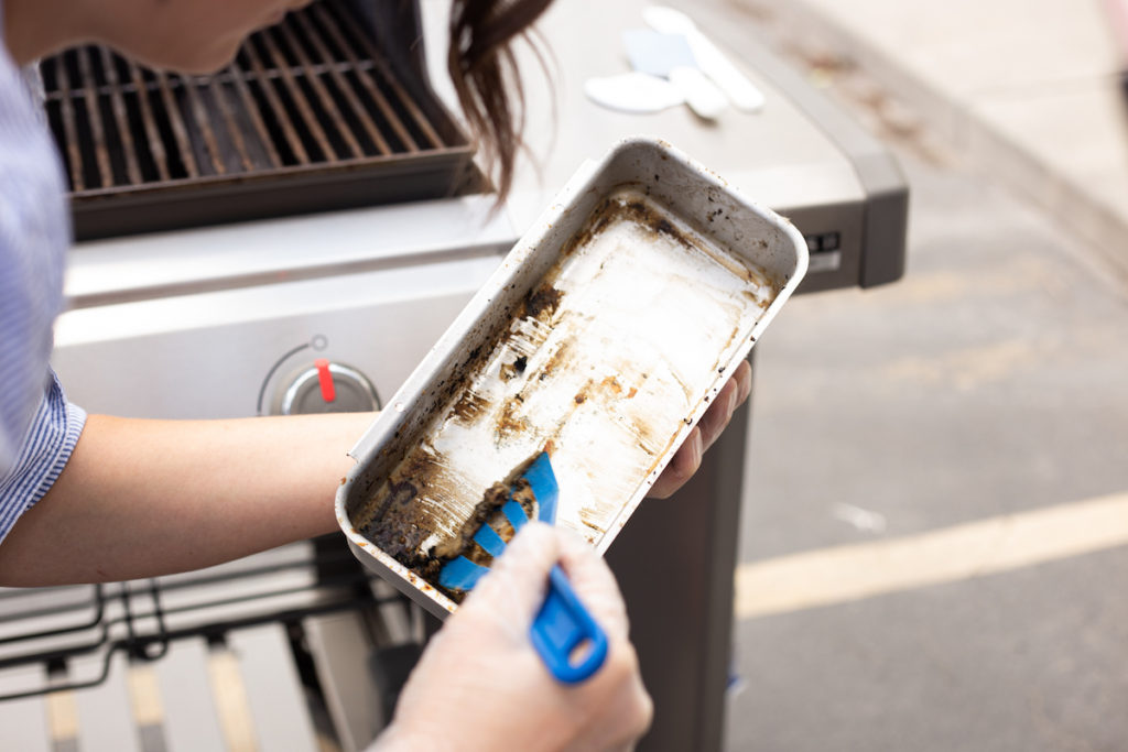 The grill grease tray is being scraped clean. 