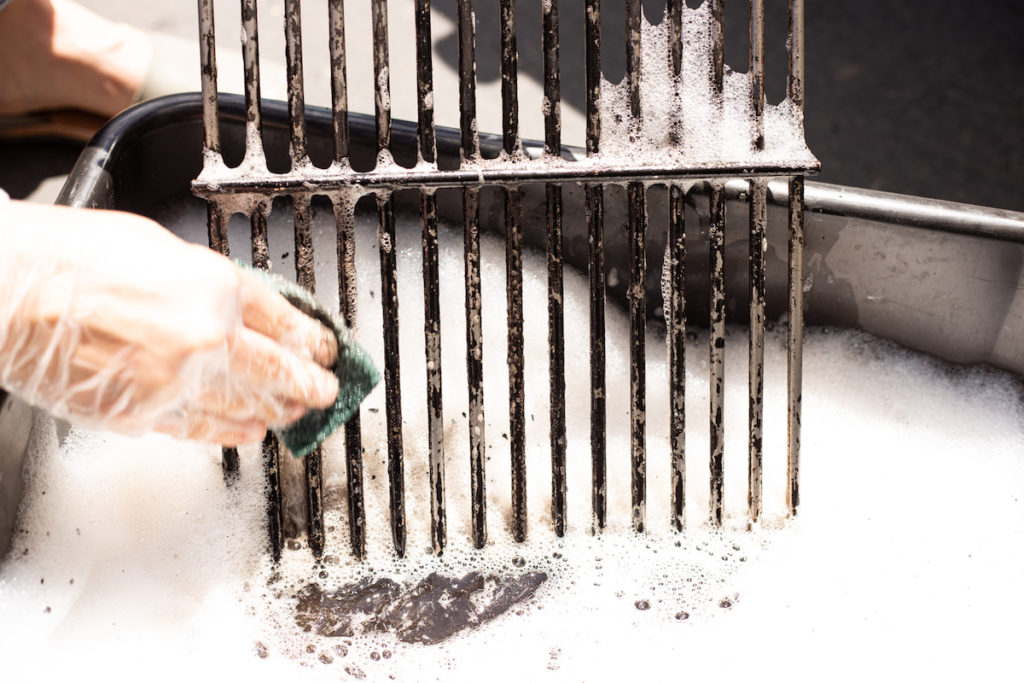 The grill grate is being scrubbed with a sponge. 