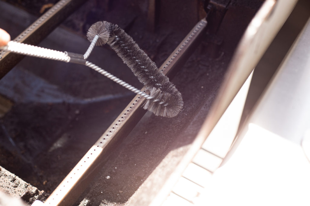 A grill brush is cleaning the grill burner tube. 