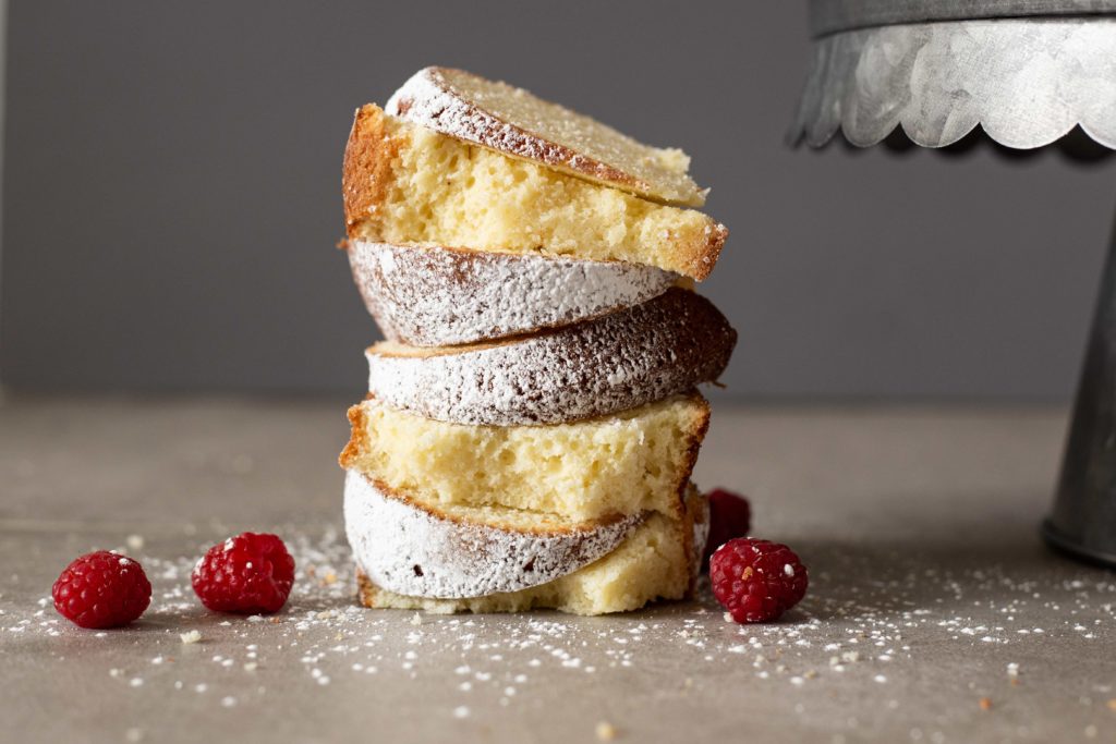 Stack of butter vanilla bundt cake slices with powdered sugar and raspberries. 