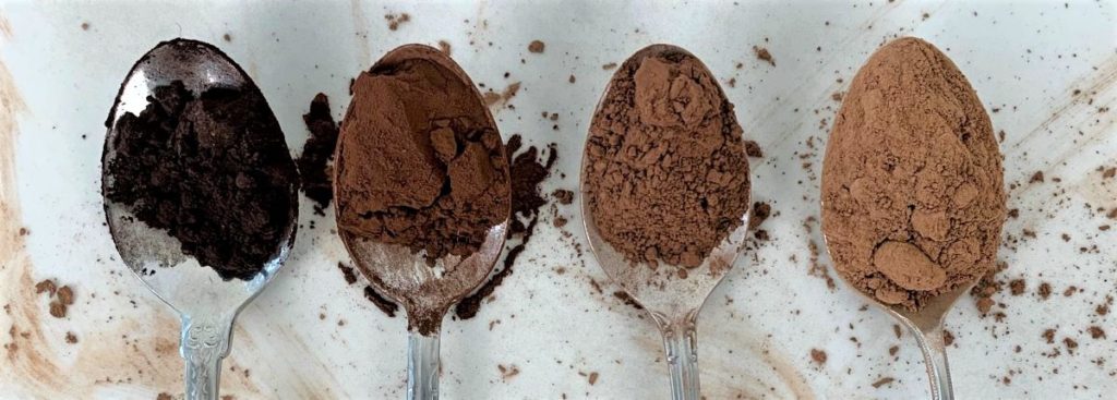 four spoons holding different colored cocoa powder 