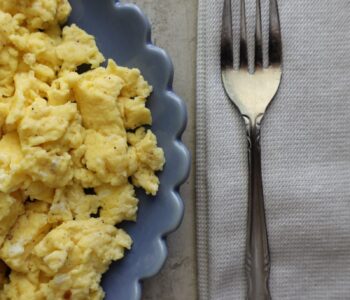 scrambled eggs on a blue scalloped plate with a fork on a cloth napkin