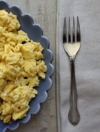 scrambled eggs on a blue scalloped plate with a fork on a cloth napkin