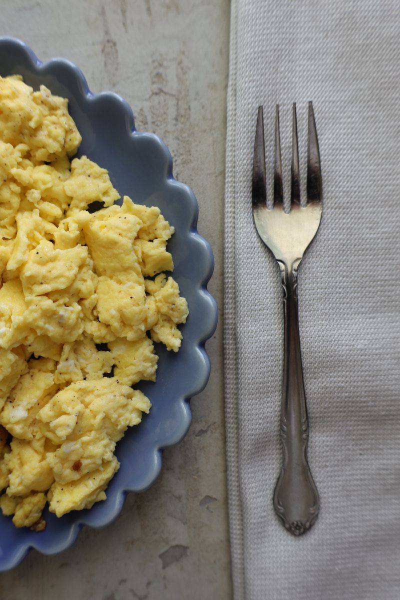 scrambled eggs on a blue scalloped plate with a fork on a cloth napkin
