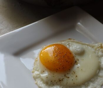 sunny side up fried egg on a square plate with enameled cast iron pan in the background