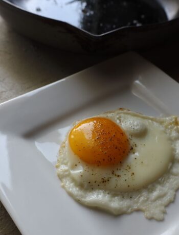 sunny side up fried egg on a square plate with enameled cast iron pan in the background