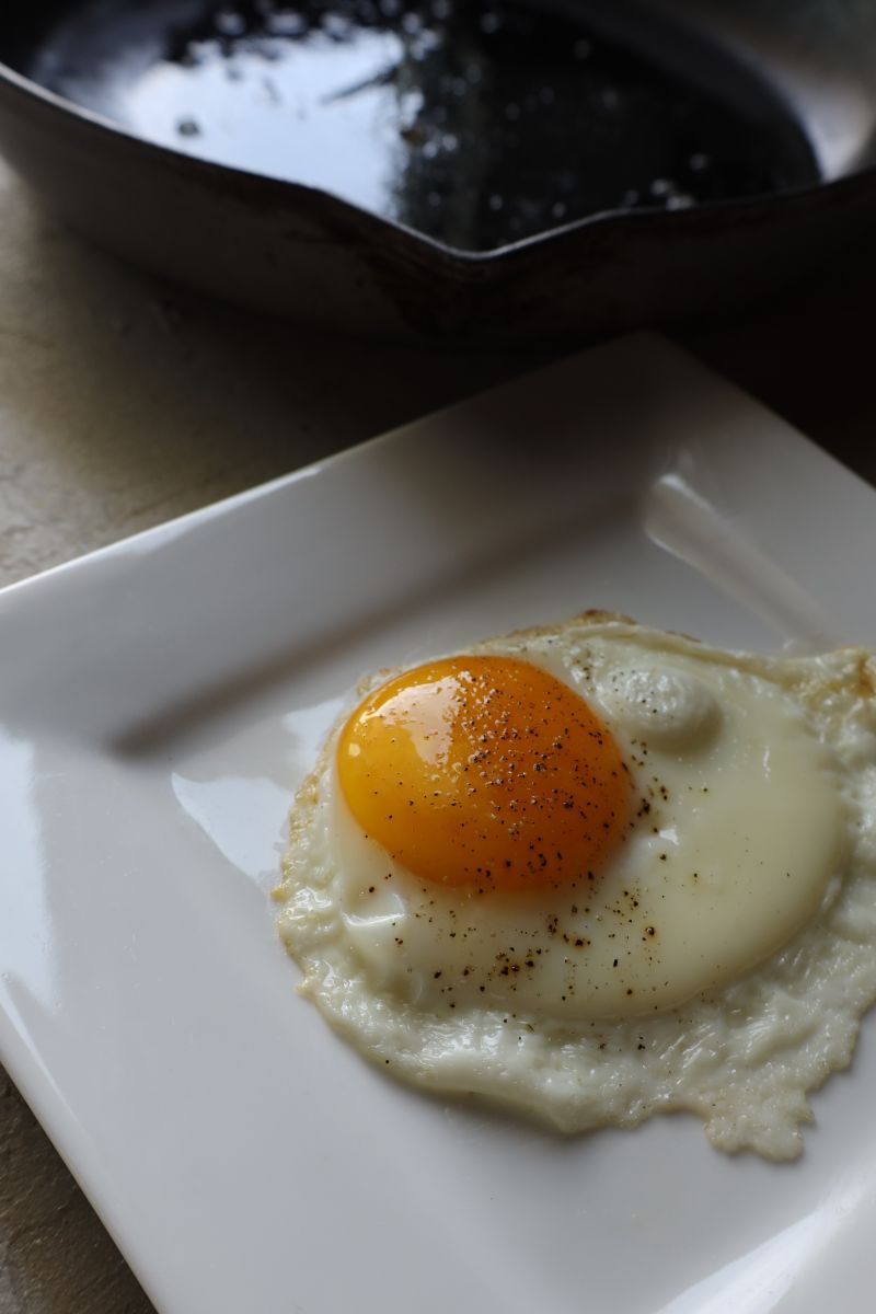 sunny side up fried egg on a square plate with enameled cast iron pan in the background
